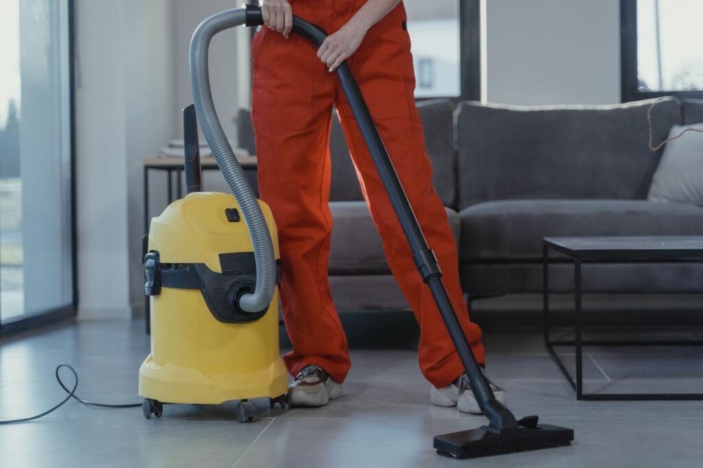 Demo Post 2 A professional cleaner in red coveralls vacuums a contemporary living room with a yellow vacuum cleaner.